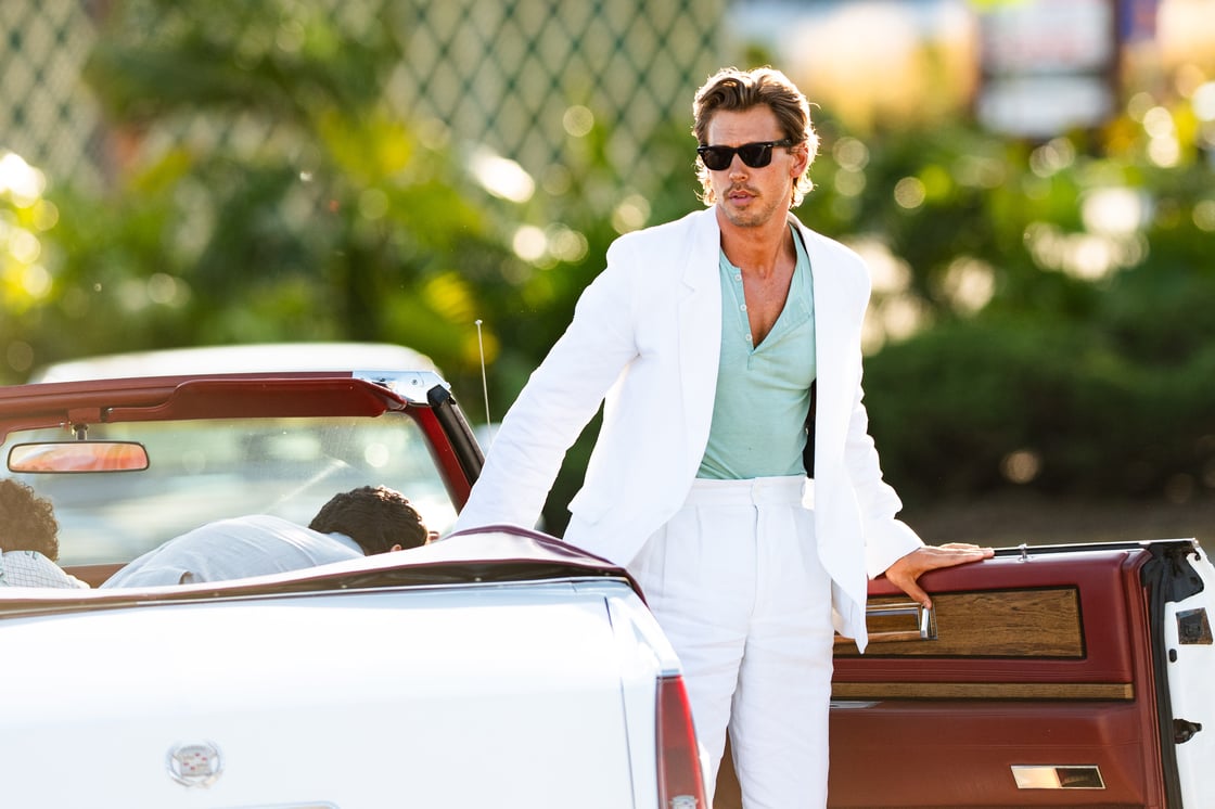Austin Butler als Sonny Crockett mit gebräunte Haut, trägt einen hellen Leinenanzug und steigt lässig aus einem weißen Cadillac